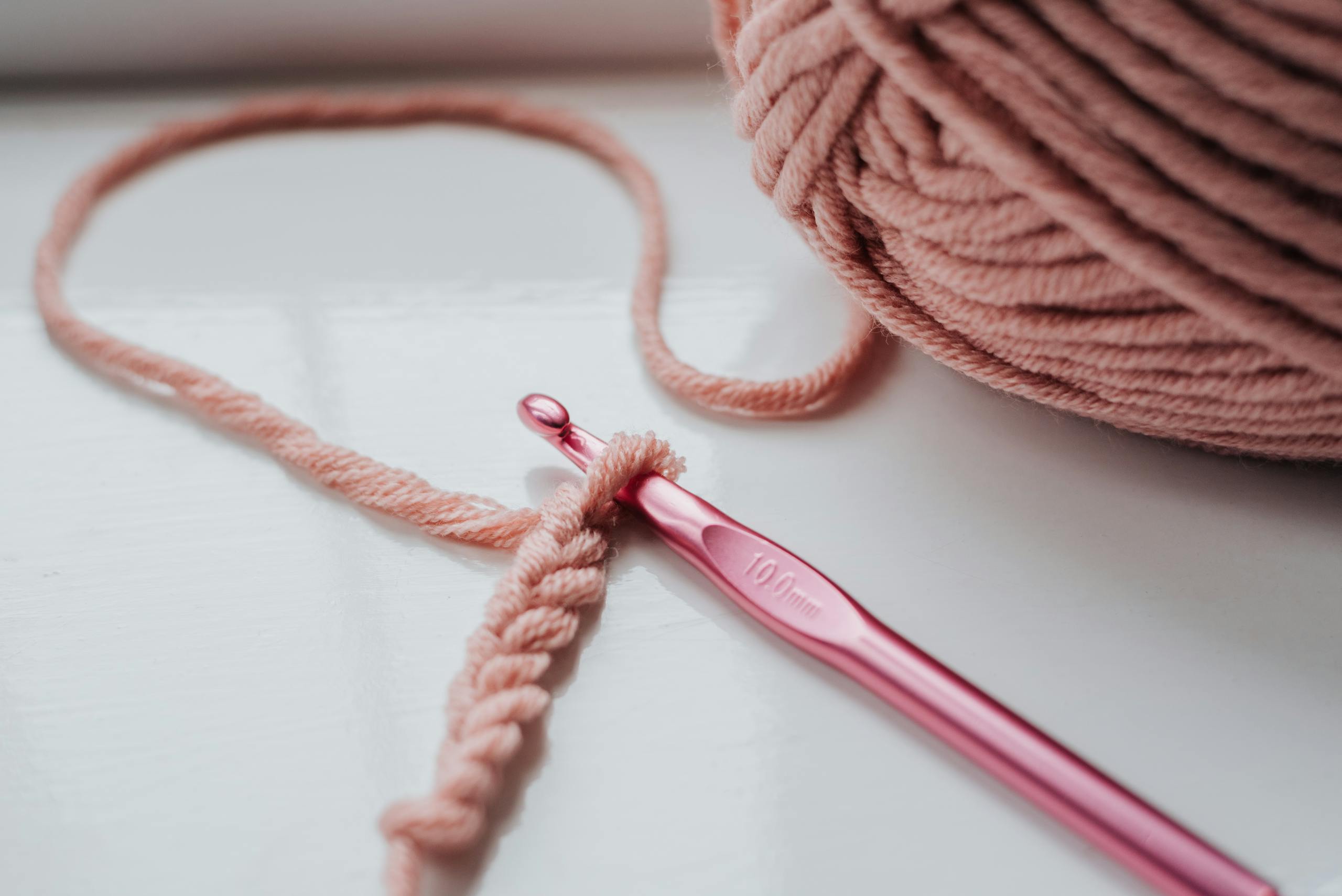 Close-up of pink yarn and crochet hook on a bright indoor windowsill, showcasing a cozy creative hobby.